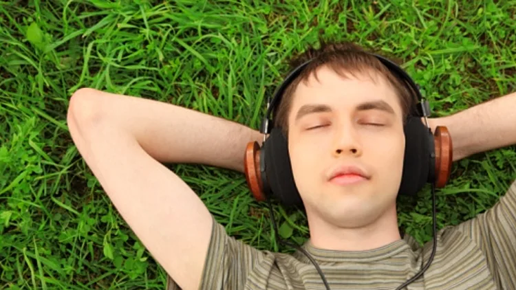 צעיר נח על הדשא עם אוזניות