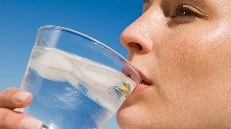 אישה שותה מים מכוס עם קוביות קרח