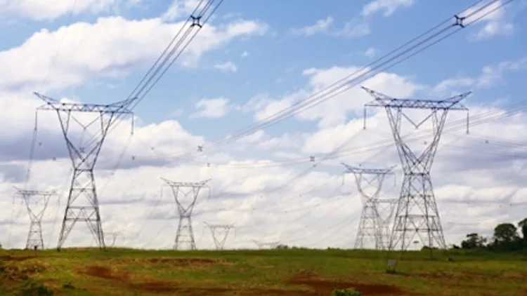 שדה עם עמודי חשמל וקווי מתח גבוה, ברקע שמים מעוננים