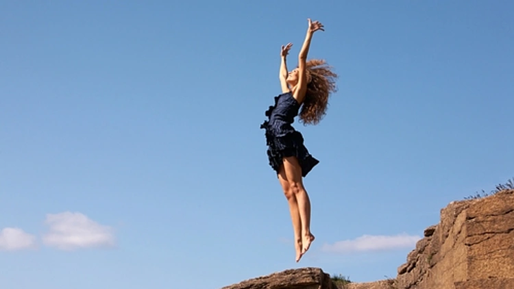 אישה עומדת על קצה צוק וקופצת באוויר