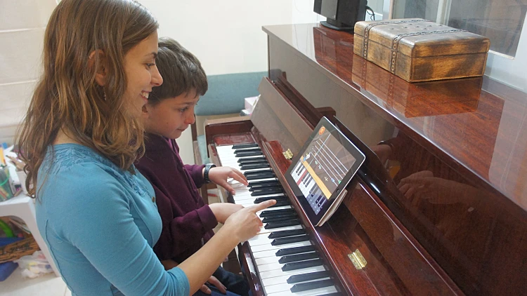 בחורה מלמדת ילד לנגן בפסנתר עם אייפד בתור לוח תווים