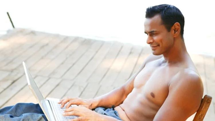 אדם עם לפ טופ שיושב על כסא בחוץ ללא חולצה