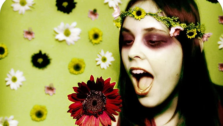 בחורה צעירה מחזיקה פרח על רקע טפט עם פרחים