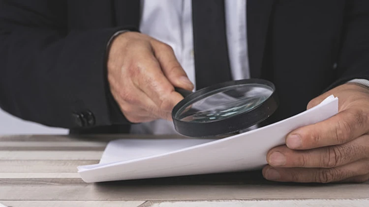 Close Up Of The Hands Of A Businessman Looking Through A Magnifying Glass For Documents