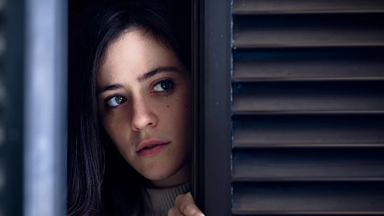 Worried,woman,watching,outside,from,a,wooden,window,shutter