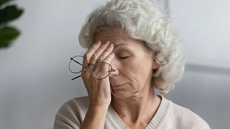 Tired,senior,lady,holding,glasses,and,rubbing,face,with,closed