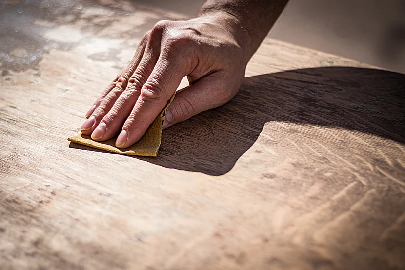 Gritty,weathered,man's,hand,and,sandpaper;,hand,sanding,a,table