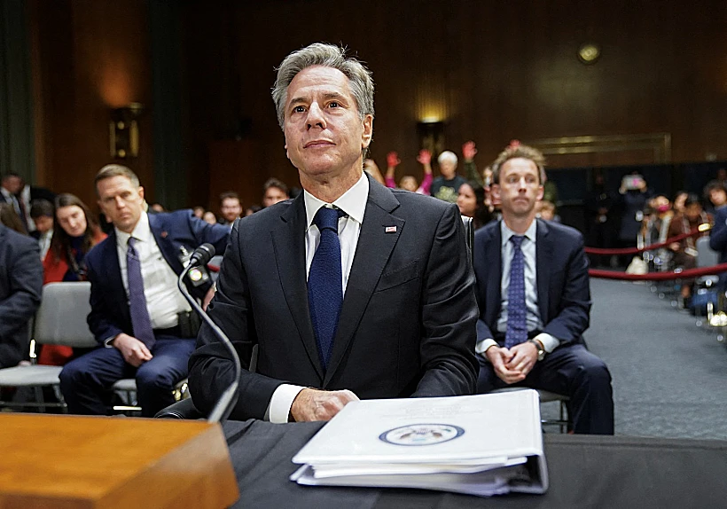 בלינקן מעיד בדיון בוועדת ההקצאות של הסנאט בגבעת הקפיטול בוושינגטון כשמאחוריו מפגינים עם ידיים צבועות באדום