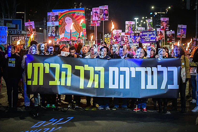 מפגינים אוחזים בשלט למען החטופים מחוץ לקריה בת"א