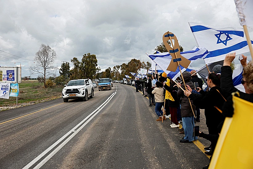 אזרחים עם דגלי ישראל מלווים את שיירת החטופים ברעים