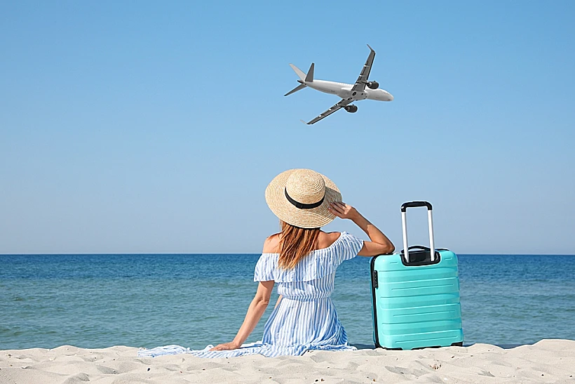 אישה בחופשה על שפת הים עם טרולי ומטוס ממריא