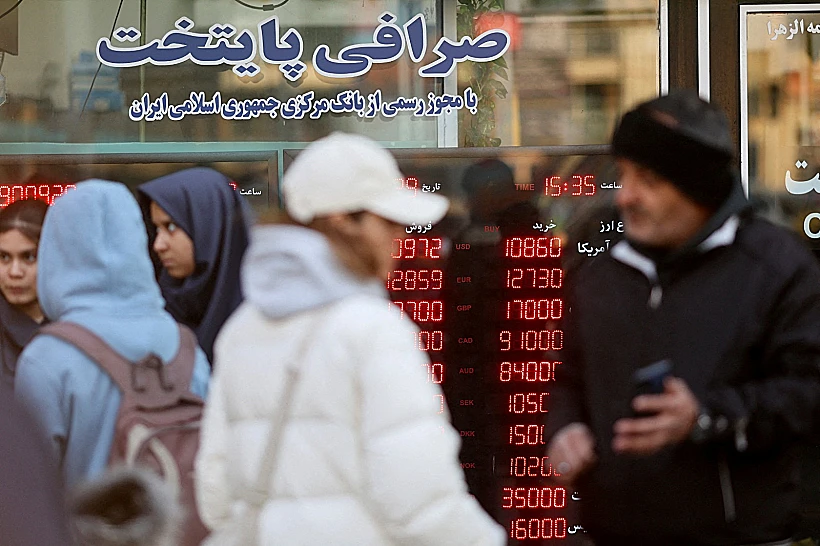 אזרחים בטהרן ברקע מסך המציג את שער המטבע שממשיך לצנוח