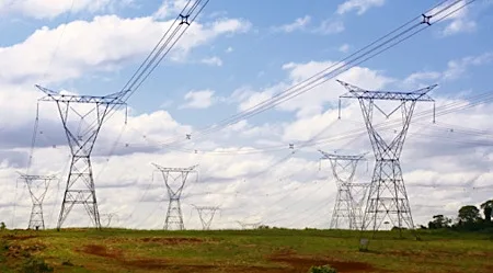 שדה עם עמודי חשמל וקווי מתח גבוה, ברקע שמים מעוננים