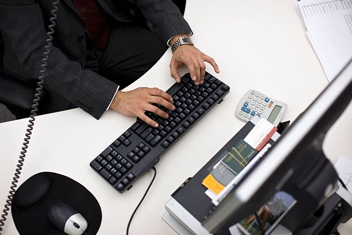 אדם מקליד מול מסך מחשב; תמונה במבט על