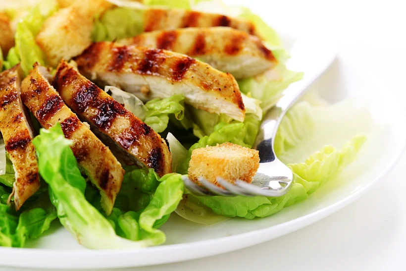 Caesar,salad,with,grilled,chicken,on,white,plate.