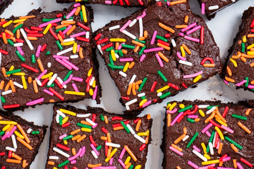 Homemade,chocolate,frosted,brownies,with,rainbow,sprinkles,on,a,white