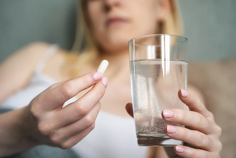 Stressed,woman,drinking,white,round,pill,while,sitting,in,bed