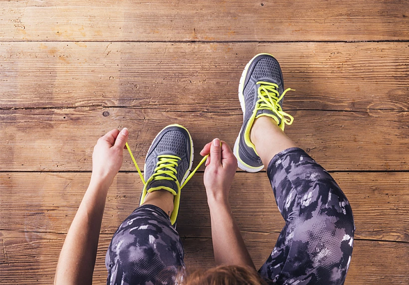 Unrecognizable,young,runner,tying,her,shoelaces.,studio,shot,on,wooden