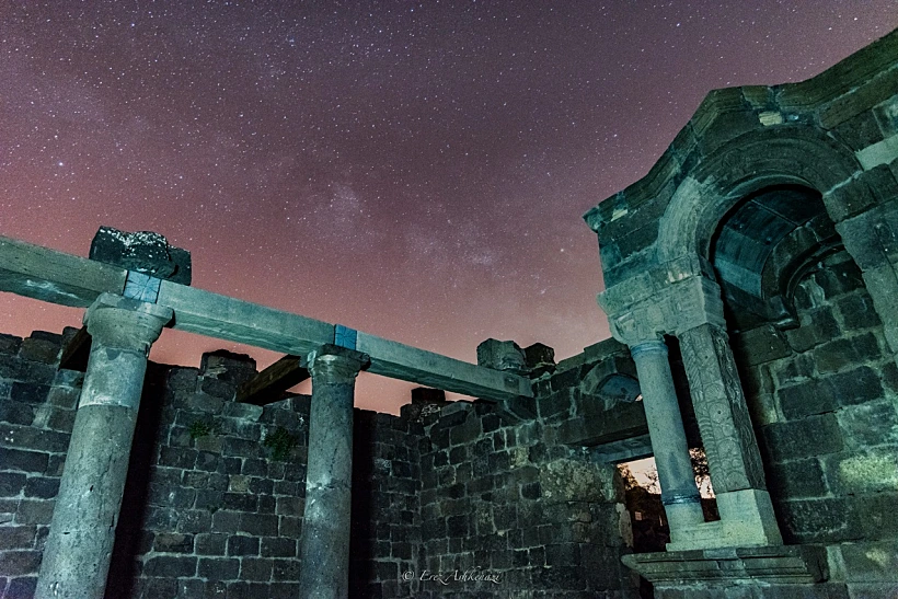 מבט על בית הכנסת העתיק באום אל-קנאטר שברמת הגולן. התמונה מציגה את חזית המבנה עם קשתות האבן המרשימות, עמודים מעוטרים ופרטים אדריכליים המעידים על פארו של בית הכנסת בתקופת התלמוד