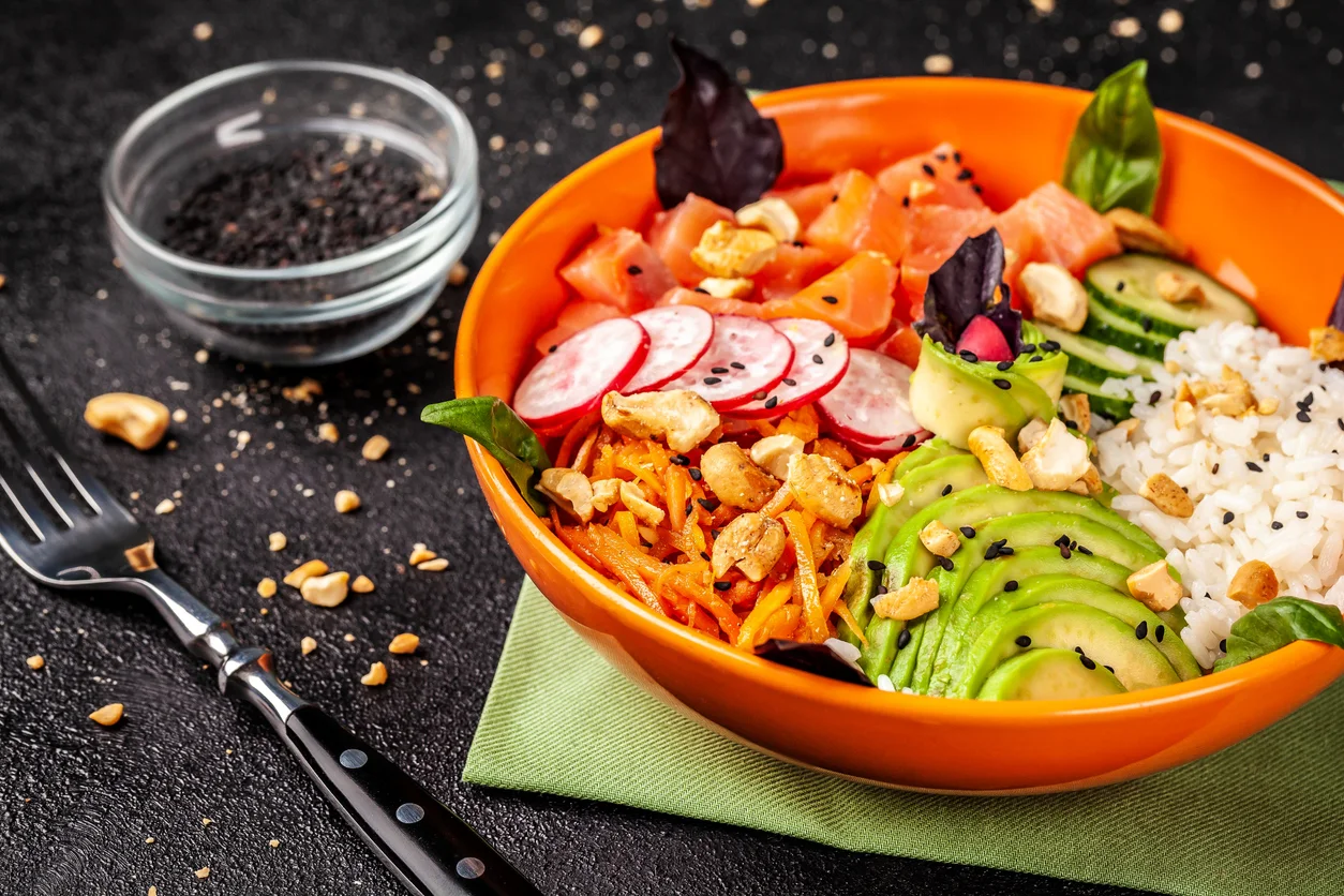 Hawaiian Salad Poke With Salmon Fish, Avocado, Korean Carrots, Cucumbers, Radish And Rice, With Black Sesame. In An Orange Plate. On The Black Background. Copy Space, Top View