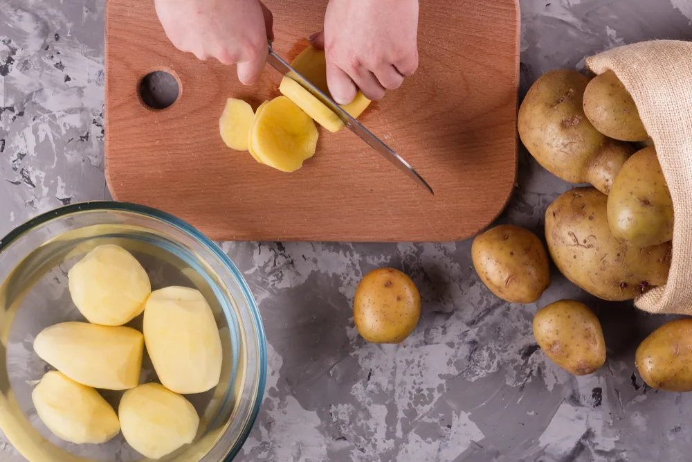Young,woman,in,an,apron,cuts,potatoes
