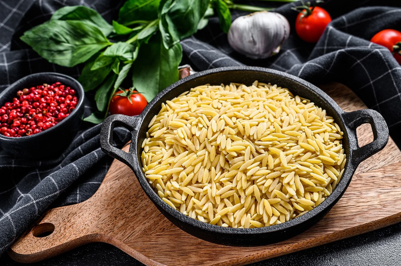 A,bowl,of,uncooked,orzo,pasta,with,basil,leaves,,tomatoes